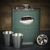 A green leather hip flask set with stainless steel cups and a pouring funnel, displayed on a dark background.